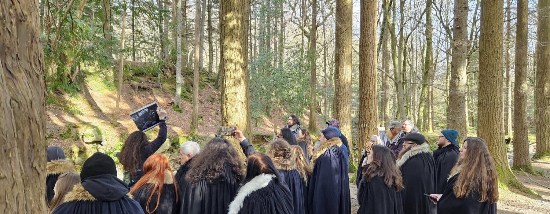 A tour group is guided through a wood wearing long black cloaks